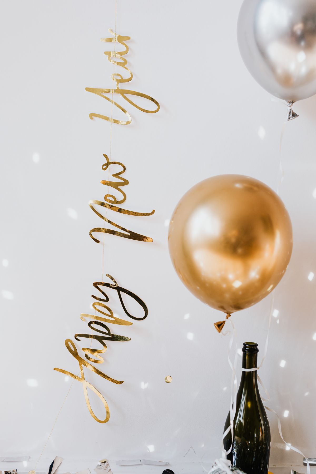 Gold Happy New Year banner, metallic balloon, and champagne bottle with ribbons on a white background